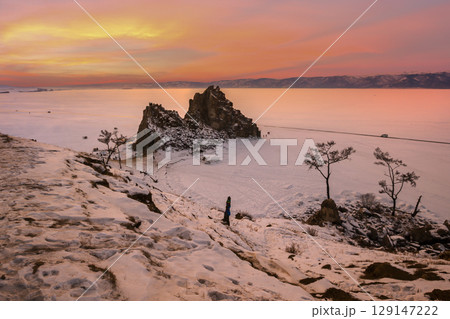 Baikal Lake in December. Magnificent sunset landscape of Olkhon Island in snowy weather. View of the natural landmark - Shamanka Rock and the Wish Tree. 129147222