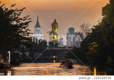 A boat was passing Big Buddha statue (Phra Buddha Dhammakaya Thepmongkhon ) in Wat Pak Nam Phasi Charoen temple located by the river during sunset. 129148556