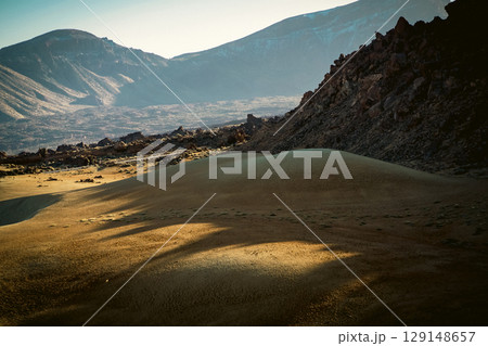 A desert landscape with sandy valleys among mountains and volcanoes at sunset. 129148657