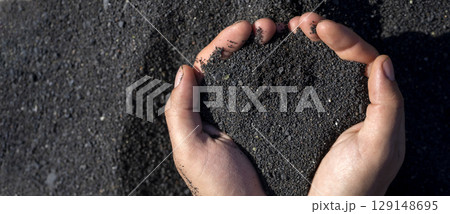 A person is holding a black volcanic sand in his or her hands, closeup view. 129148695