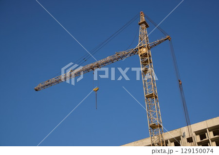 A tall crane under a clear blue sky symbolizes progress in construction and urban growth 129150074