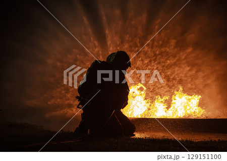 Firefighter training, fireman using water and extinguisher to fighting with fire flame in an emergency situation., under danger situation all firemen wearing fire fighter suit for safety. 129151100