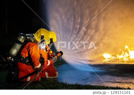 Firefighter training, fireman using water and extinguisher to fighting with fire flame in an emergency situation., under danger situation all firemen wearing fire fighter suit for safety. Firefighter training, fireman using water and extinguisher to fighting with fire flame in an emergency situation., under danger situation all firemen wearing fire fighter suit for safety. 129151101