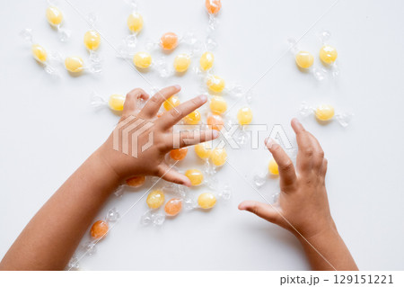 Child hands reaching for wrapped yellow and orange hard candies on white surface 129151221