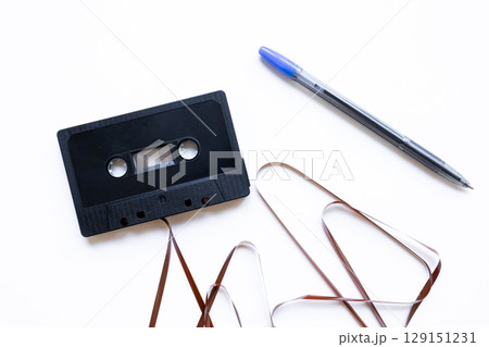 Retro black cassette tape with unraveled tape beside a blue pen on white background Retro black cassette tape with unraveled tape beside a blue pen on white background 129151231