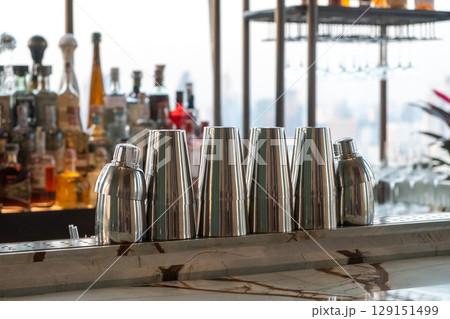 Set of cocktail shakers on the counter bar, with blurred image of various drinks on the background 129151499