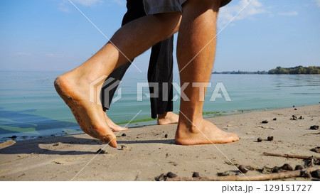 Bare feet of couple stepping together along sand beach at coastline. Male and female legs of pair walking near seaside. Happy lovers going along sandy shore. Concept of summer vacation or holiday Bare feet of couple stepping together along sand beach at coastline. Male and female legs of pair walking near seaside. Happy lovers going along sandy shore. Concept of summer vacation or holiday 129151727