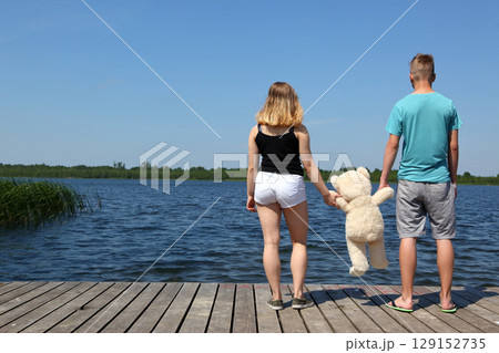 A Couple Happily Holding Hands by the Peaceful Lake, Enjoying Time with a Teddy Bear 129152735