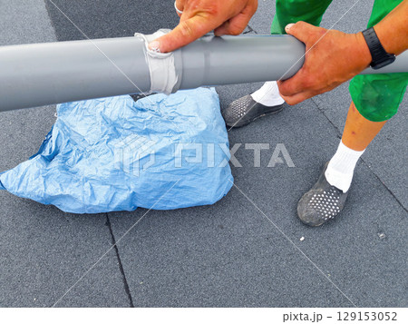 A diligent man is skillfully handling a pipe on the roof while carrying a blue bag 129153052