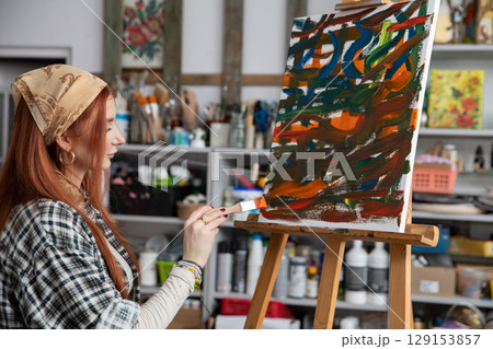 A Female Artist Diligently Painting in a Vibrant and Colorful Studio Space Filled with Inspiration A Female Artist Diligently Painting in a Vibrant and Colorful Studio Space Filled with Inspiration 129153857