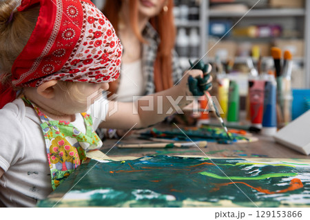 A Creative Child Enthusiastically Painting with Their Mother in a Vibrant Art Studio 129153866