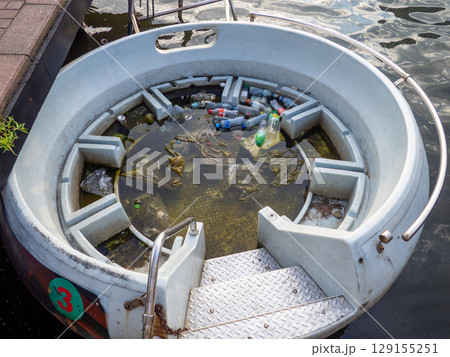 Half-submerged pleasure boat. Dirt and plastic bottles in the water. Ecological catastrophy. Environmental problems. Garbage in the water. 129155251