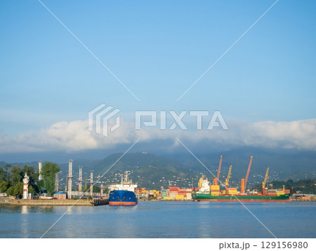 Landscape in the seaport. Port in the Caucasus. Ships and mountains. Clouds over the mountains. Port in Batumi. Logistics. Black Sea cargo transportation industry Landscape in the seaport. Port in the Caucasus. Ships and mountains. Clouds over the mountains. Port in Batumi. Logistics. Black Sea cargo transportation industry 129156980