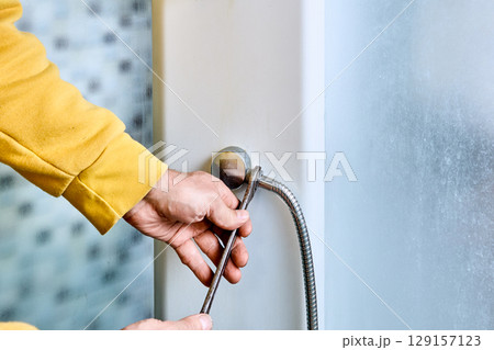 Flexible shower hose connection process shows installer tightening hose onto shower mixer outlet using open-end wrench with clear detail of threading at attachment point. 129157123