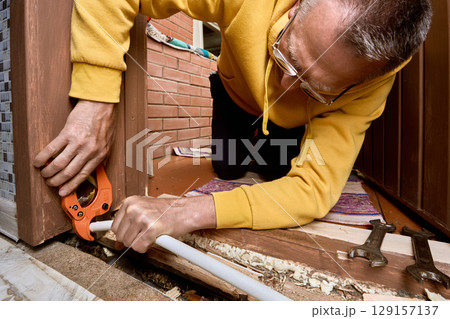 Pipe is being cut with ratchet cutter by plumber to prepare clean edge on multilayer tubing before installation of compression fitting coupling. 129157137