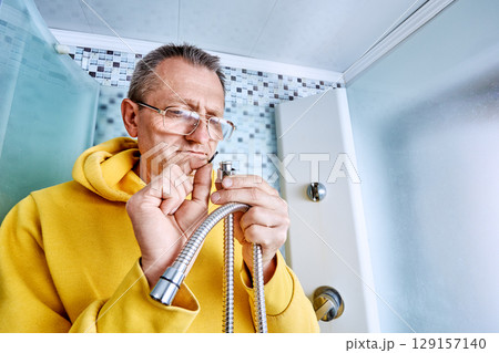 Replacing sealing ring on braided shower hose, plumber inserts new gasket into connector while standing inside shower stall during repair process. Replacing sealing ring on braided shower hose, plumber inserts new gasket into connector while standing inside shower stall during repair process. 129157140