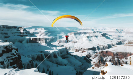 Paraglider soaring above snowy canyon landscape with clear blue sky and expansive mountain views Paraglider soaring above snowy canyon landscape with clear blue sky and expansive mountain views 129157280