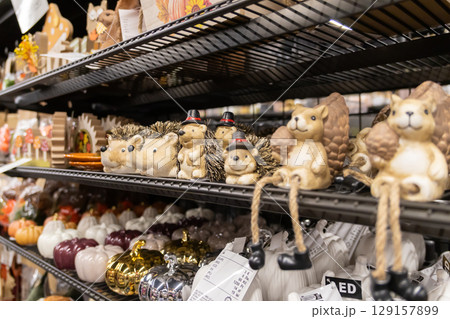 Retail shelves showcasing decorative autumn ornaments, featuring charming hedgehog figurines wearing tiny hats, playful squirrels, and a variety of colorful pumpkins Retail shelves showcasing decorative autumn ornaments, featuring charming hedgehog figurines wearing tiny hats, playful squirrels, and a variety of colorful pumpkins 129157899