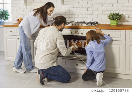 Father pulling baked muffins from oven standing in modern kitchen cooking with family at home 129160788
