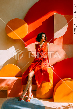 A woman in a red dress is sitting on a yellow and orange sculpture A woman in a red dress is sitting on a yellow and orange sculpture 129161173