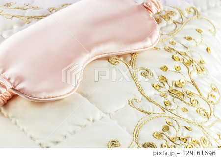 Sleep mask on a white silk pillow with embroidery. Insomnia or depression treatment. luxury bed linen. Pleasant sleep and relaxing at home concept with soft luxury cushion 129161696