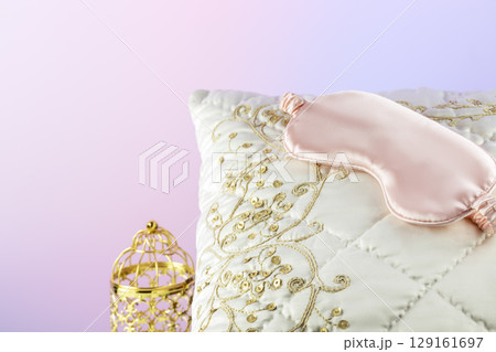 White silk pillow with pink sleep mask and golden candlestick on a gradient background. luxury bed linen. Pleasant sleep and relaxing at home concept with soft luxury cushion White silk pillow with pink sleep mask and golden candlestick on a gradient background. luxury bed linen. Pleasant sleep and relaxing at home concept with soft luxury cushion 129161697