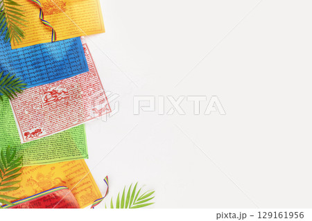 Colorful Buddhist Tibetan prayer flags, Lungta with, Om Mani Padme Hum, mantra prayer on a white background with palm leaves and copy space. Buddhist religion holiday background Colorful Buddhist Tibetan prayer flags, Lungta with, Om Mani Padme Hum, mantra prayer on a white background with palm leaves and copy space. Buddhist religion holiday background 129161956