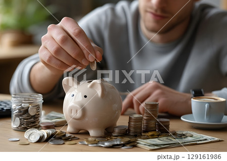 A hand drops a coin into a classic piggy bank, symbolizing smart financial planning and the habit of saving money. A hand drops a coin into a classic piggy bank, symbolizing smart financial planning and the habit of saving money. 129161986