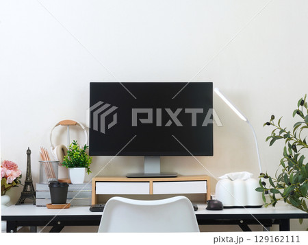 Stylish and organized workspace with monitor, desk lamp, headphones, flowers, and Eiffel Tower decor. Stylish and organized workspace with monitor, desk lamp, headphones, flowers, and Eiffel Tower decor. 129162111