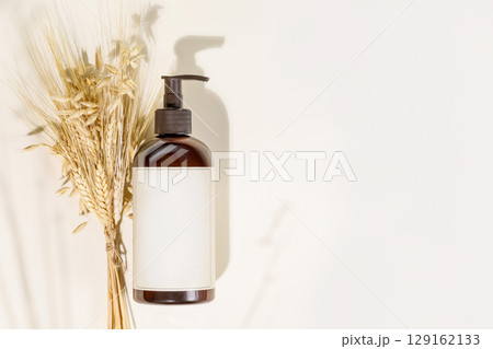 Natural beauty product. Mockup. Dispenser bottle with beauty product on a light background with rye and wheat bouquet and copy space. Mock up of natural washing gel. Flat lay 129162133