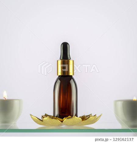 Amber glass dropper bottle with serum, essential oil or fruit peeling on a glass shelf on a blue background with candles. SPA natural organic cosmetic, aroma oil for skin. Front view. Mockup concept Amber glass dropper bottle with serum, essential oil or fruit peeling on a glass shelf on a blue background with candles. SPA natural organic cosmetic, aroma oil for skin. Front view. Mockup concept 129162137
