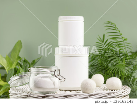 Natural laundry detergent mockup. Washing detergent concept with bottles of washing gel or fabric softener on a white laundry basket on a green background with house plants. Laundry day 129162148