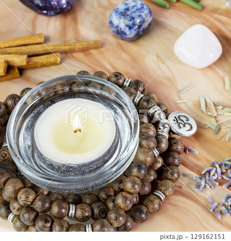 Self-care, healing composition with rosary beads, chakra stones, sandalwood sticks and candle on a pink marble podium. Concept of relaxing at home, energy healing, yoga, meditation and me time 129162151