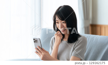 ソファに座ってスマートフォンを使う笑顔の女性 ソファに座ってスマートフォンを使う笑顔の女性 129162175