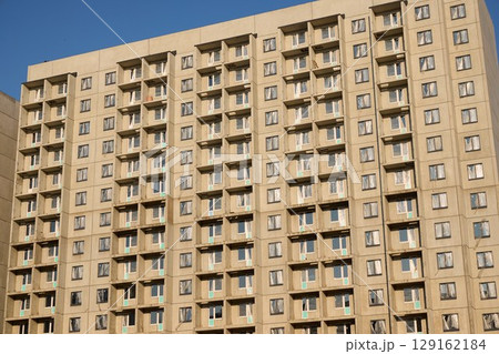 A sleek, modern apartment building stands prominently against a beautiful clear sky backdrop A sleek, modern apartment building stands prominently against a beautiful clear sky backdrop 129162184