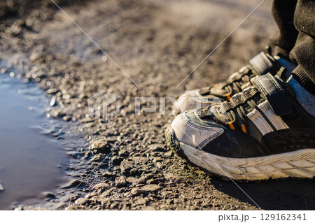 Close-up of children's dirty sneakers next to a puddle 129162341