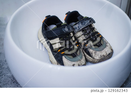 Children's dirty sneakers are lying in a white sink. Mud after a walk 129162343