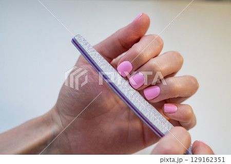 Woman with pink nail polish filing her nails with a nail file, close-up shot. Self-care and beauty concept 129162351
