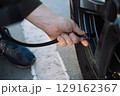 Person's hand inflating a car tire with an air compressor, checking pressure 129162367