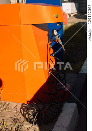 Vibrant orange air pump station for tire inflation with a pressure gauge and black hose Vibrant orange air pump station for tire inflation with a pressure gauge and black hose 129162368