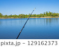 Fishing rod extends towards the water on a sunny day, capturing a beautiful outdoor scene 129162373