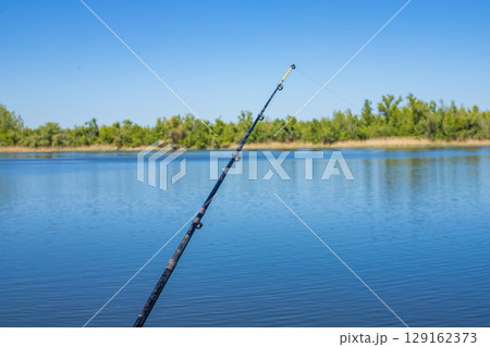 Fishing rod extends towards the water on a sunny day, capturing a beautiful outdoor scene 129162373