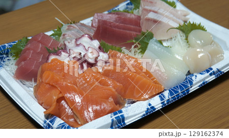 プラスチック容器に美しく盛り付けられた新鮮なマグロ、サーモン、イカなどの刺身盛り合わせ 129162374