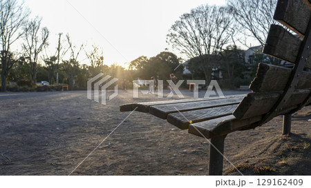 夕日が差し込む公園のベンチと、遠くで遊ぶ子ども達のシルエット 夕日が差し込む公園のベンチと、遠くで遊ぶ子ども達のシルエット 129162409