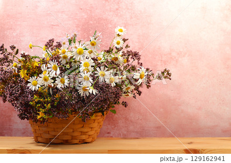 A flower arrangement of wild medicinal herbs on a wooden table in a basket, a bouquet of St. John's wort, oregano, mint, chamomile, a collection of useful herbs for treatment according to folk recipes A flower arrangement of wild medicinal herbs on a wooden table in a basket, a bouquet of St. John's wort, oregano, mint, chamomile, a collection of useful herbs for treatment according to folk recipes 129162941