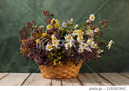 Flower arrangement of wild medicinal herbs on a wooden table in a basket, a bouquet of St. John's wort, oregano, mint, chamomile, a collection of useful herbs for treatment according to folk recipes Flower arrangement of wild medicinal herbs on a wooden table in a basket, a bouquet of St. John's wort, oregano, mint, chamomile, a collection of useful herbs for treatment according to folk recipes 129162942