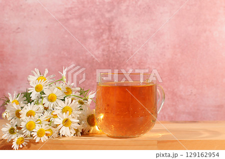 Chamomile tea or infusion in transparent glasses with natural small chamomile flowers on wooden table, concept of medicinal herbal tea and proper natural nutrition, summer postcard Chamomile tea or infusion in transparent glasses with natural small chamomile flowers on wooden table, concept of medicinal herbal tea and proper natural nutrition, summer postcard 129162954