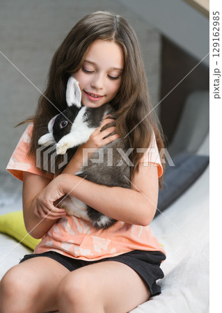 Smiling girl hugging black and white rabbit indoors. Smiling girl hugging black and white rabbit indoors. 129162985