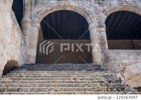 Historic stone courtyard with arched staircases, ancient sculptures in a Mediterranean old town 129163097