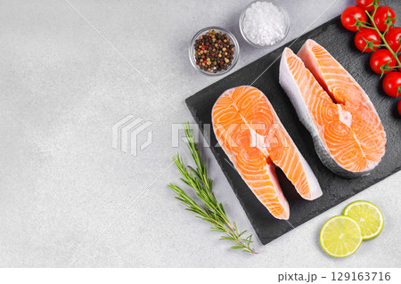 Two fresh raw salmon, trout steak with tomatoes, spices, rosemary and lime on white stone background 129163716